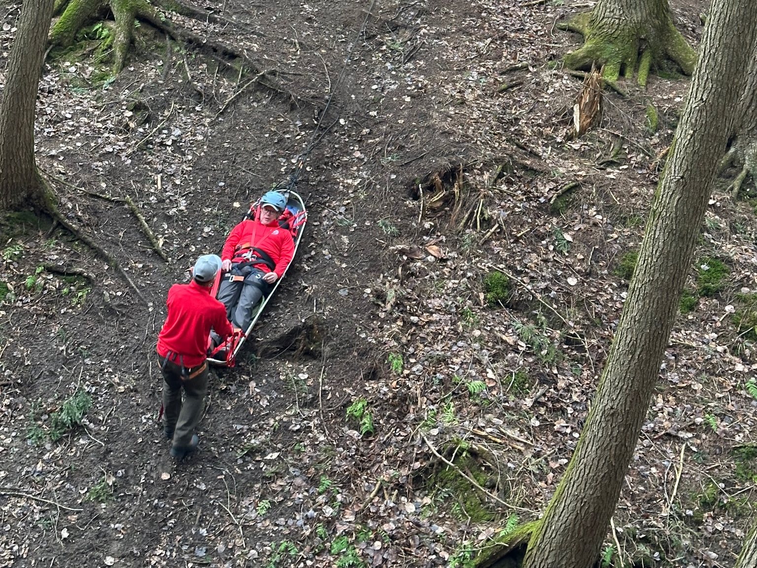 A KSAR member tends a litter with a volunteer patient on a steep slope while teammates work the rope system above